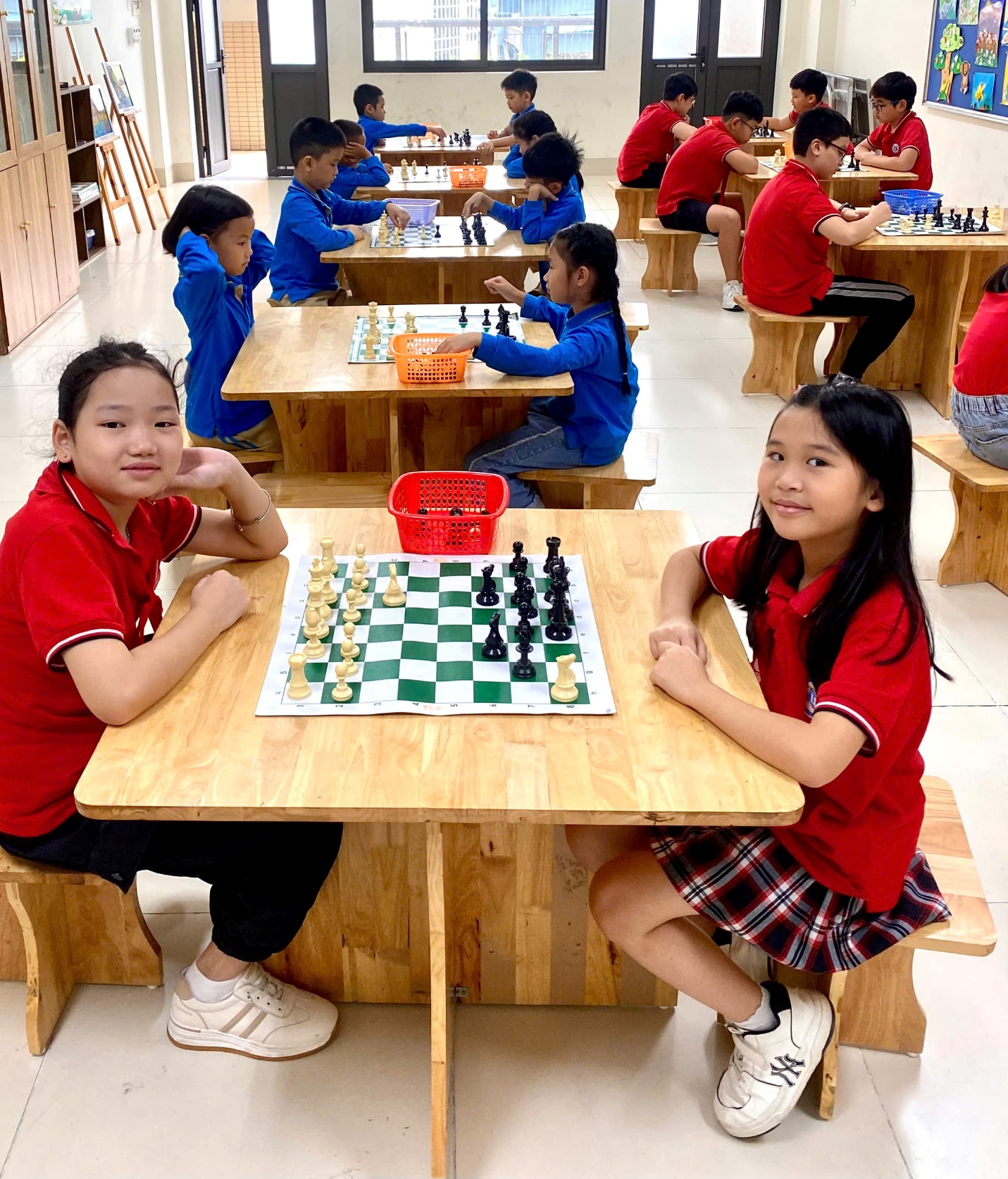 A group of kids sitting at tables with chess board
Description automatically generated