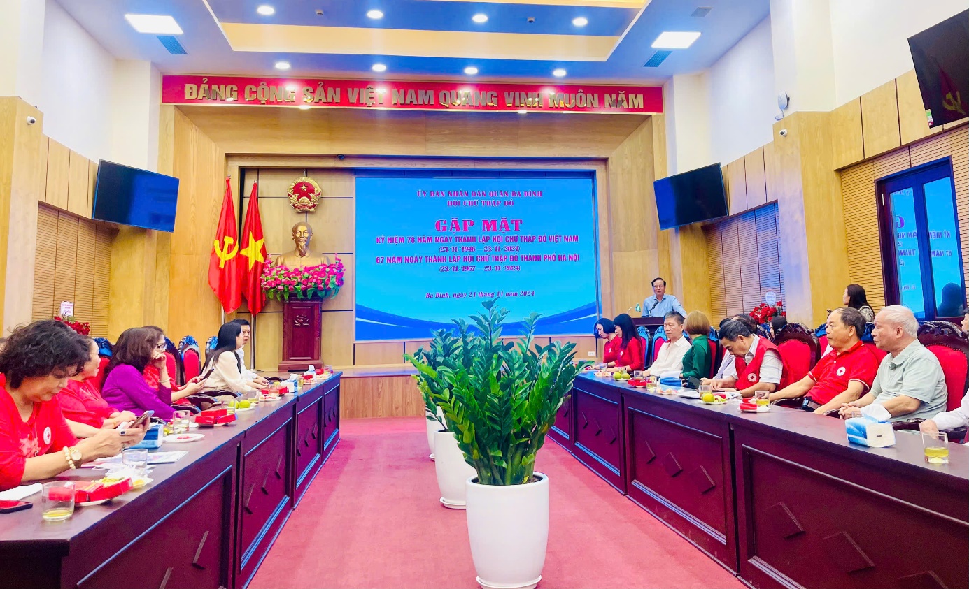A group of people sitting at long tables in a room with a large screen
Description automatically generated