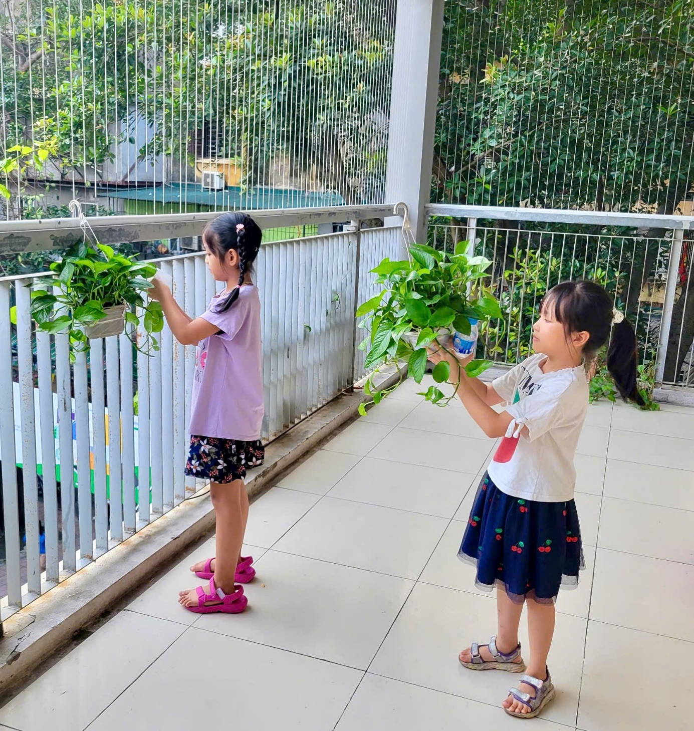 Two girls holding plants on a balcony
Description automatically generated